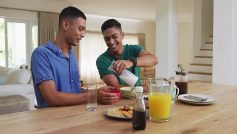 Smiling-mixed-race-gay-male-couple-having-breakfast-together-in-kitchen