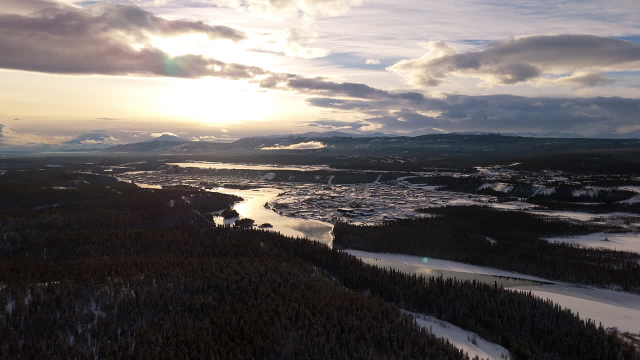 A smooth aerial shot of the rugged Yukon landscape at sunset, highlighting Downtown Whitehorse and the winding Yukon River in this breathtaking view of the northern wilderness.