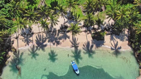 tropical paradise lagoon with sand beach and blue boat, top down aerial forward