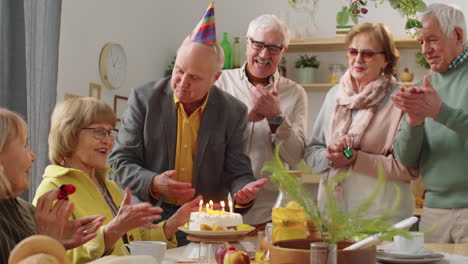 Fröhliche-ältere-Frau-Bläst-Kerzen-Auf-Geburtstagstorte-Zum-Abendessen-Mit-Freunden