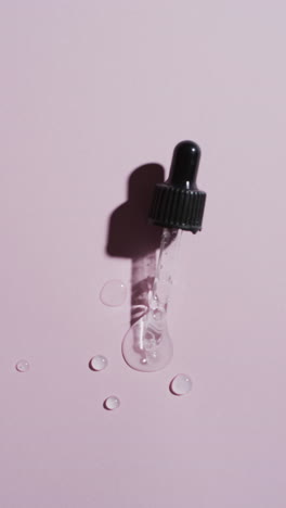 vertical video of make up pipette and drops of serum with copy space on pink background