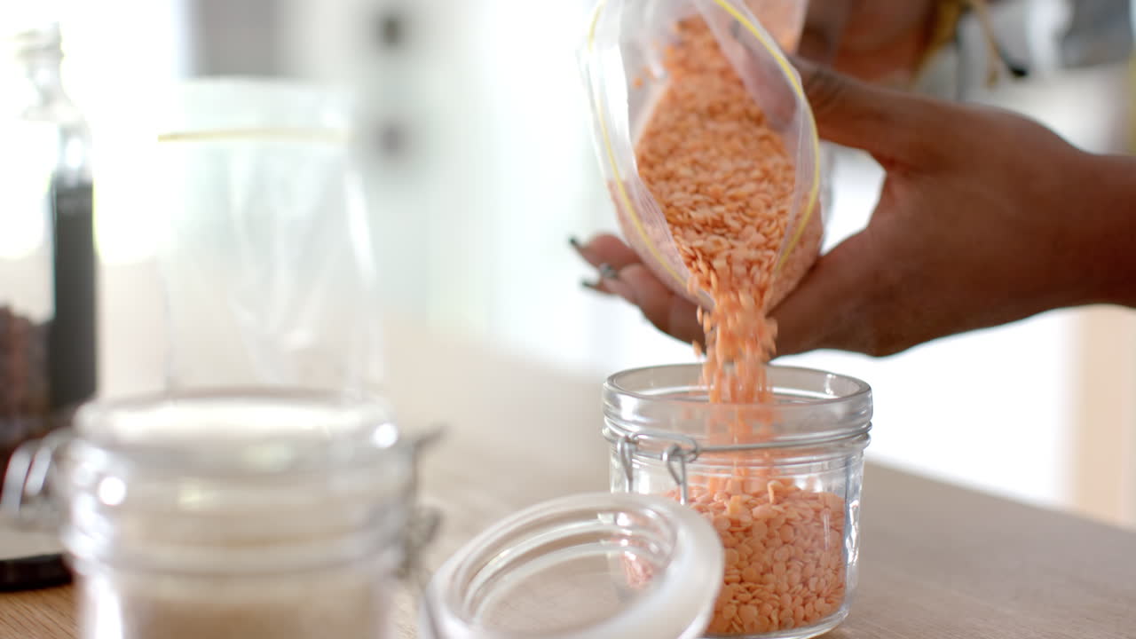 Pouring lentils into glass jar, person organizing pantry in kitchen