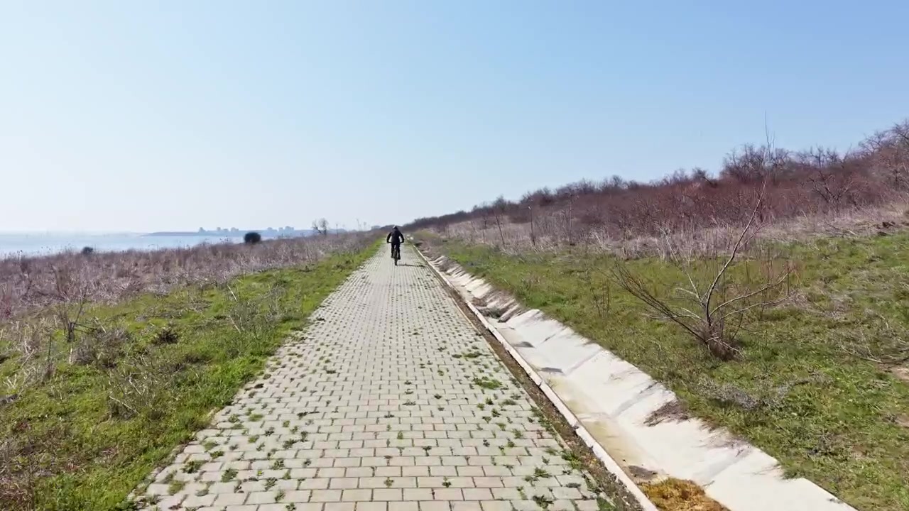 맑고 화창한 날, 자전거 타는 사람이 물가 근처 야외 길을 따라 자전거를 타고 있습니다.
