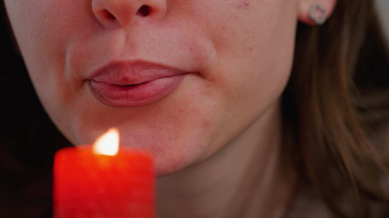 primer plano de una vela roja ardiente siendo apagada por una mujer con labios pintados, el suave resplandor de la llama contrasta con el calor de su aliento mientras se prepara para apagarla