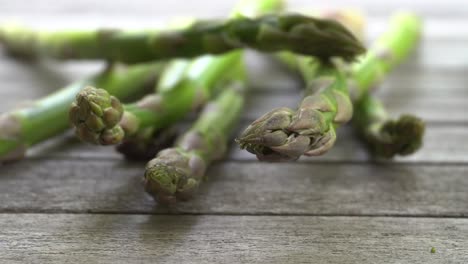 Aufnahmen-Von-Einem-Bund-Frischer,-Grüner-Spargel,-Der-Auf-Einen-Holztisch-Fällt