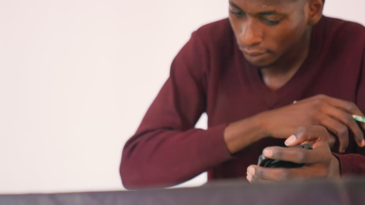 Black man sketching from phone reference, using phone image for portrait study, focused gaze, pencil marks on paper, studio indoor setting, creator balancing analog and digital, thoughtful practice