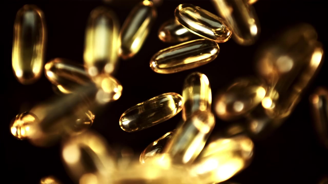 Capsule softgel dorate che cadono al rallentatore su sfondo nero