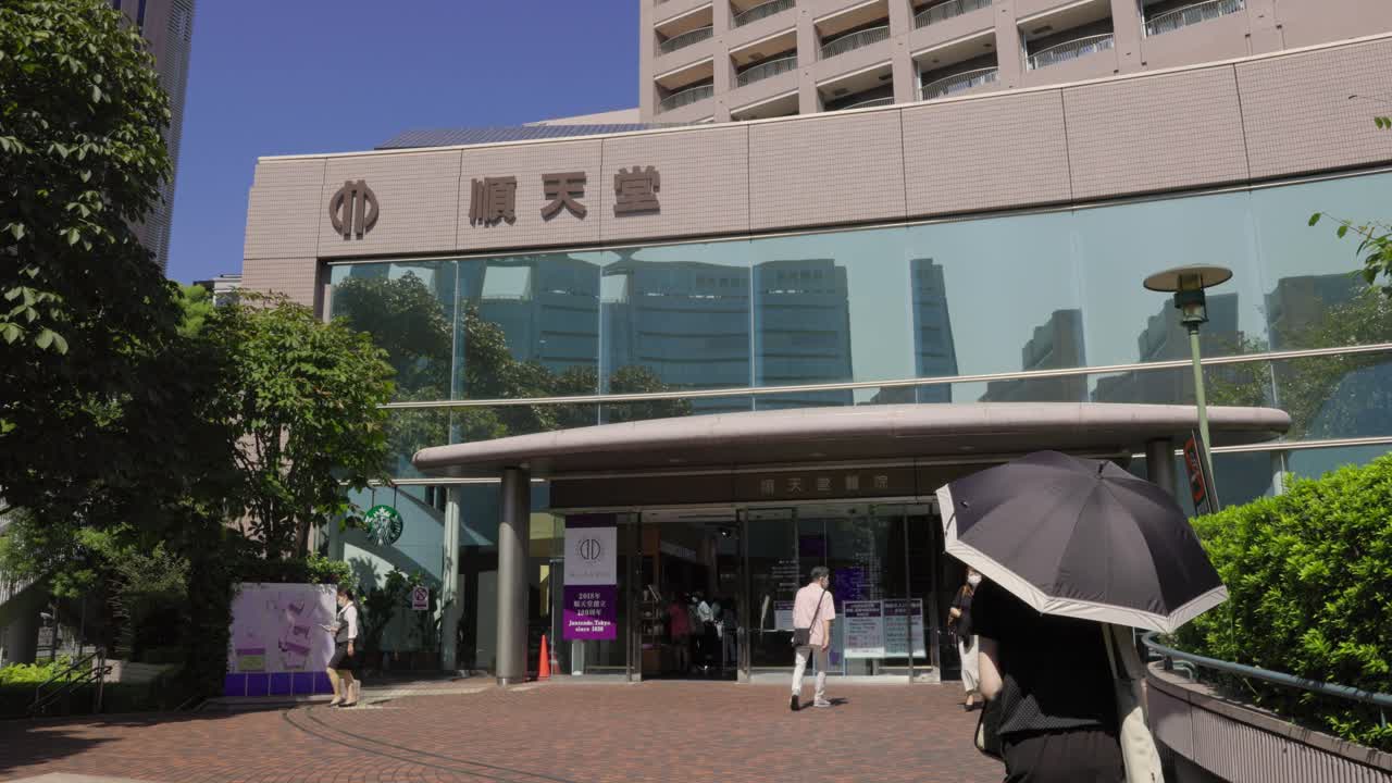 People walking toward the entrance of a Tokyo hospital on a bright sunny day