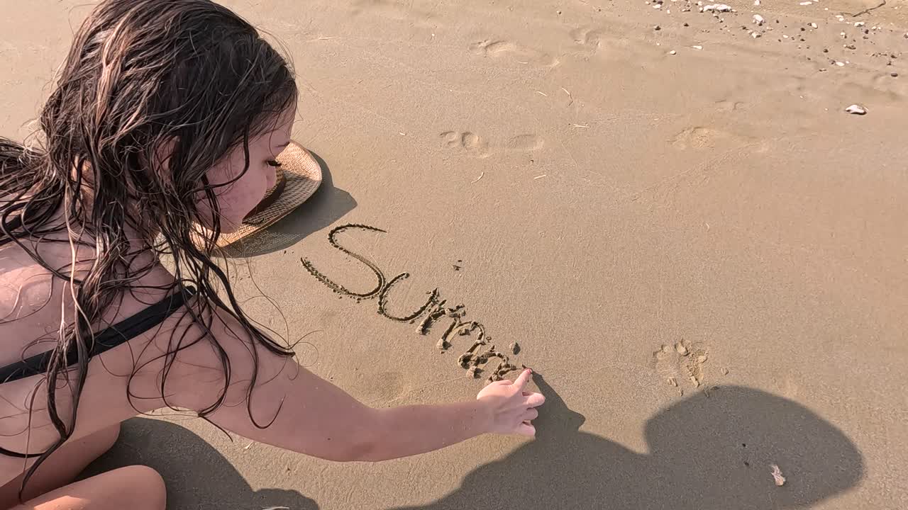 Joyful moments unfold as a young girl interacts with the warm sand, using a hat to create captivating shadows on the beach. Laughter and adventure fill the sunny atmosphere