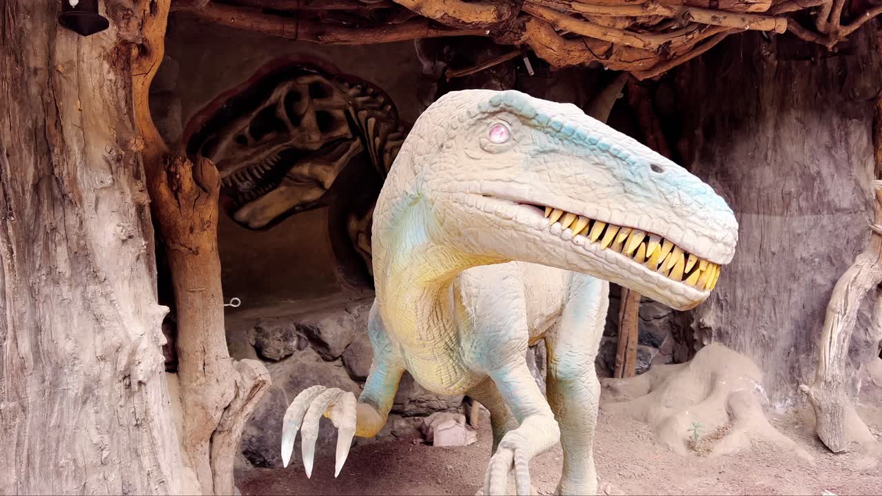 A close-up image shows a display featuring a dinosaur model with yellow teeth and a skeleton in a simulated rock wall and cave environment, creating an educational exhibit.