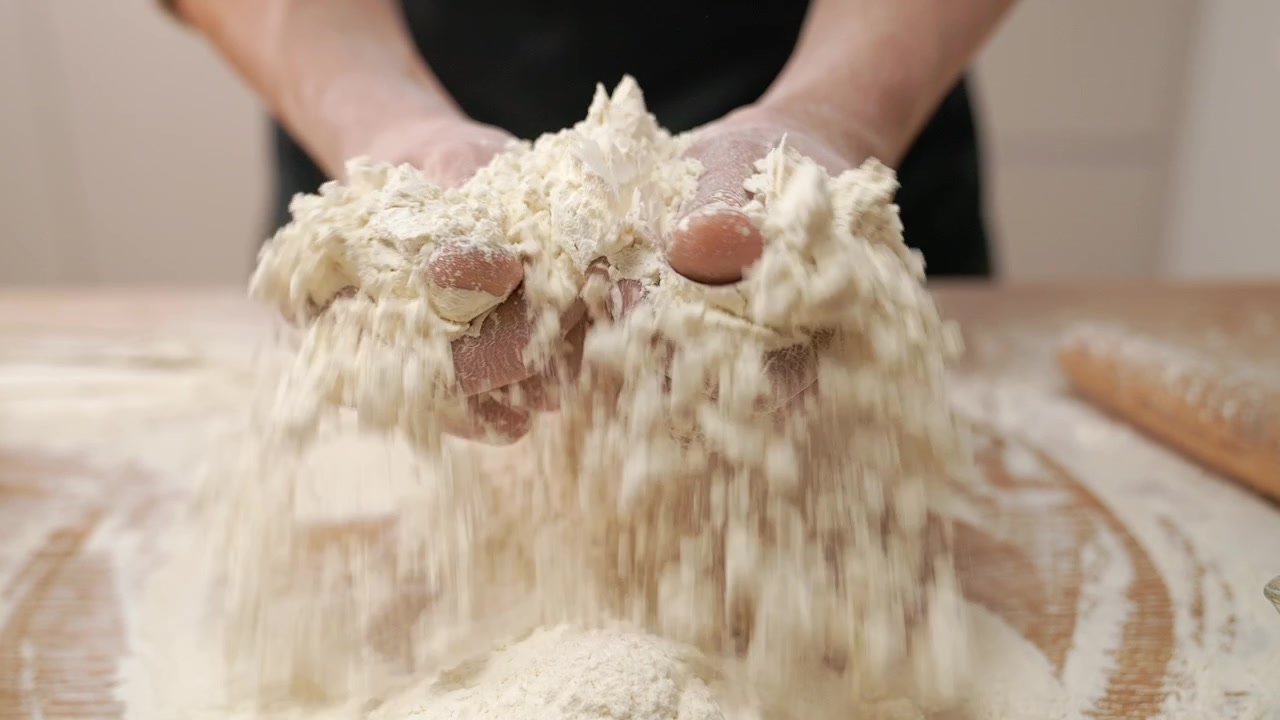 Primo piano di mani che setacciano la farina su un tavolo di legno