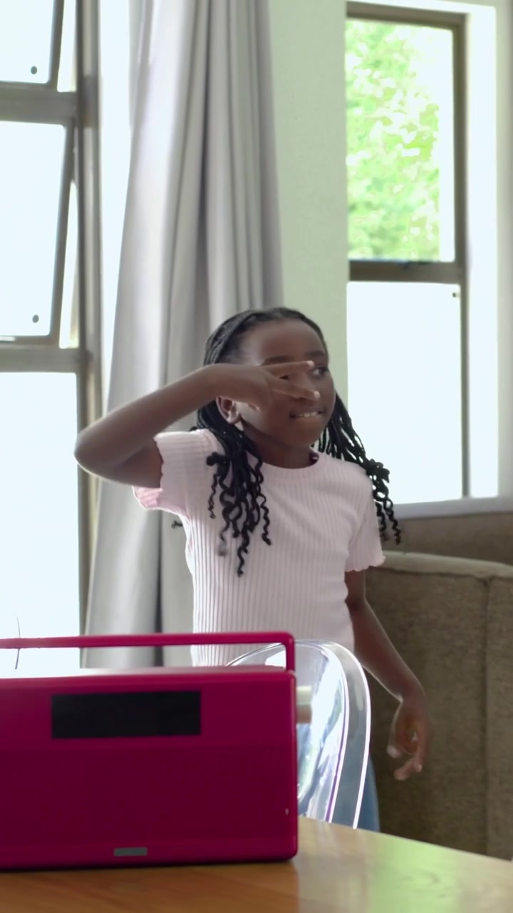 Vertical video: Dancing braided girl wearing pink top and jeans at home, following pink radio beat