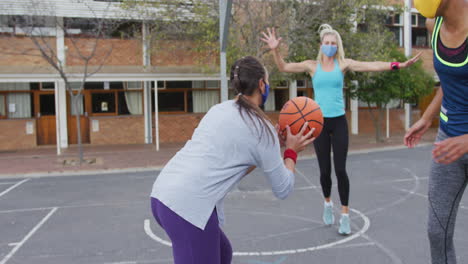 diverse female basketball team wearing face masks playing match, scoring goal