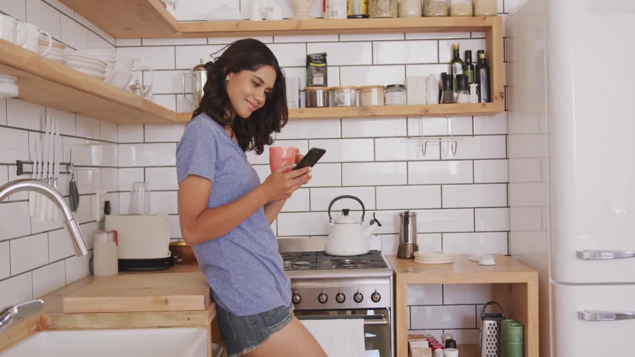 Donna allegra con una tazza di caffè che usa lo smartphone in cucina
