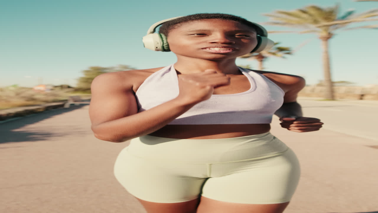 Giovane donna afroamericana che corre all'aperto con le cuffie in una giornata di sole