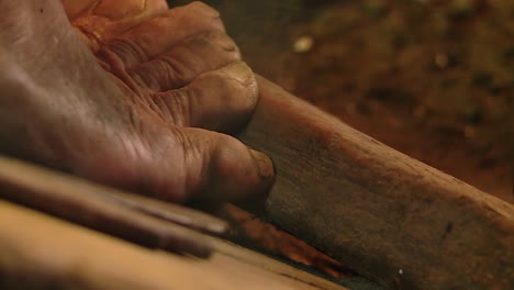 old man moving bare feet over a piece of wood while working close to a fire in traditional blacksmith oven, close up