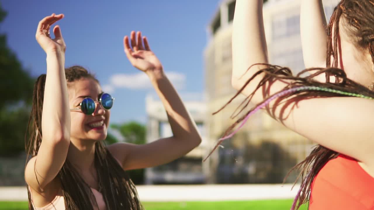 mujeres felices con dreads sentadas en la hierba en el parque de verano. amigos jóvenes hablando, bailando y jugando al aire libre divirtiéndose