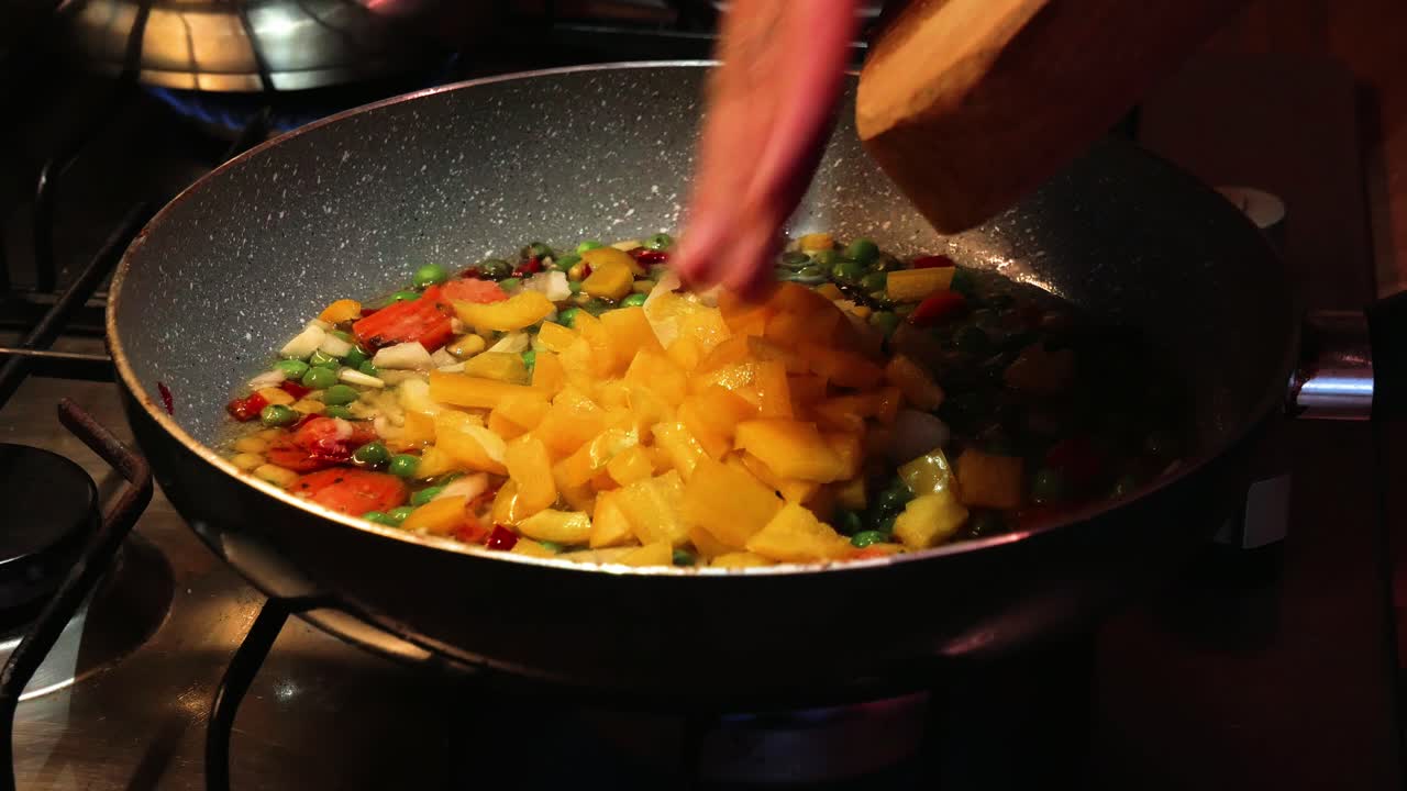 verter pimiento amarillo recién picado sobre verduras en una sartén caliente de una tabla de cortar de madera
