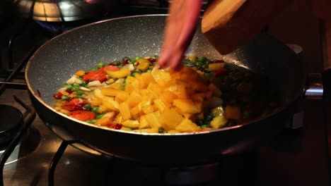 verter pimiento amarillo recién picado sobre verduras en una sartén caliente de una tabla de cortar de madera