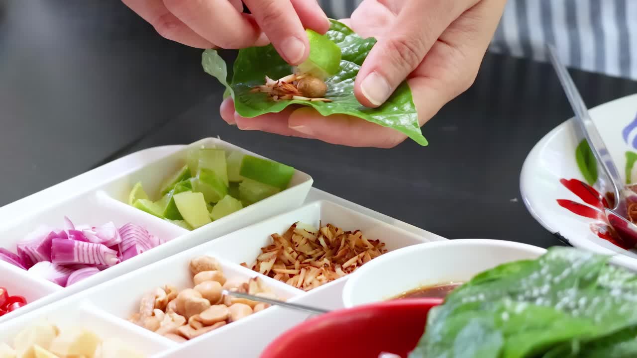 Hands skillfully prepare leaf wraps using fresh ingredients like peanuts, onions, and dried shrimp.