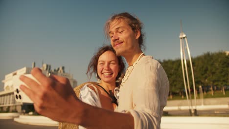 a guy holds a phone in his hands and takes a selfie with his girlfriend who kisses him on the cheek on a modern beach in the summer at sunrise. happy guy and girl on a date taking a selfie