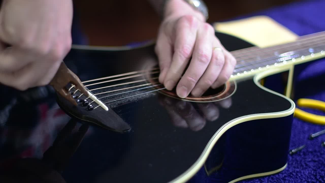 Restringing and cleaning a beautiful black single cutaway accoustic guitar - tight view of using pliers to remove the plugs locking the strings in pace