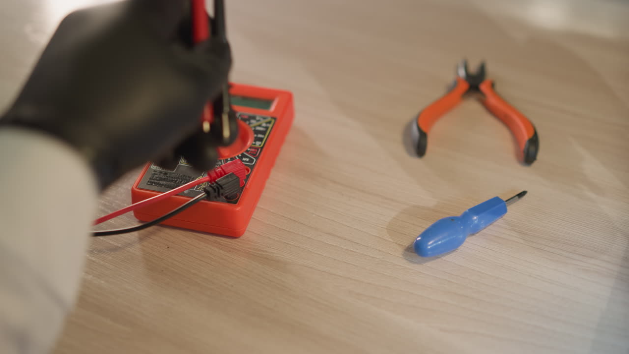 una vista de cerca de un técnico en una bata de laboratorio blanca y guantes de mano negros ajustando el voltímetro, con otras herramientas en la mesa