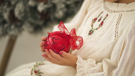 una joven con un vestido blanco adornado con navidad sosteniendo una bola roja - primer plano