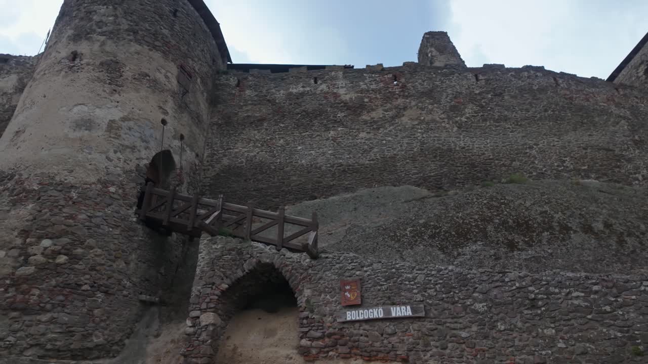 Sideways tracking shot of Boldogkő Castle in Boldogkőváralja, Hungary, highlighting its medieval stone walls, fortress towers, and historic architectural features amidst a scenic natural backdrop