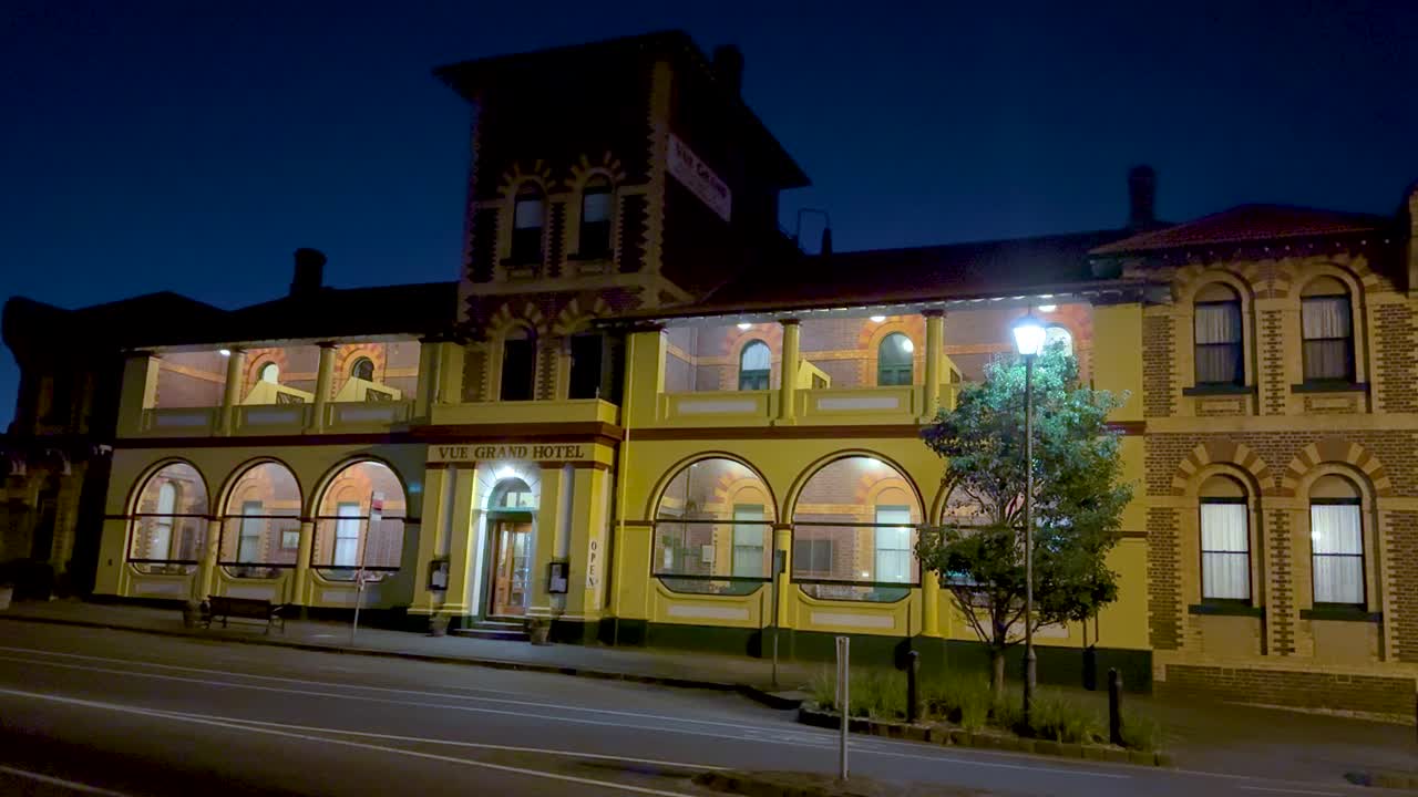 A serene nighttime scene of the Vue Grand Hotel in Queenscliff, Australia, showcasing its illuminated facade and quiet street