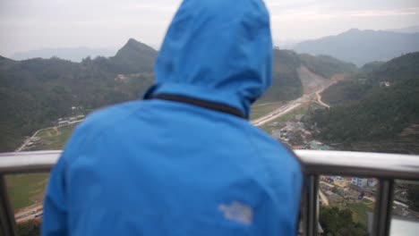 person in a blue jacket standing on top of watch tower looking down over valley in vietnam