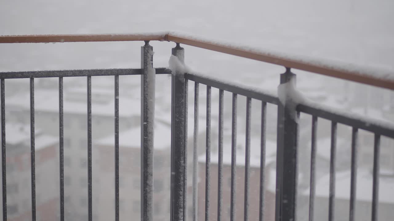 Neve che cade su un parapetto di un balcone in una scena invernale urbana