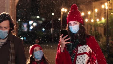 크리스마스에 눈이 내리는 동안 거리에서 스마트폰으로 입력하는 행복한 아름다운 젊은 여성의 초상화