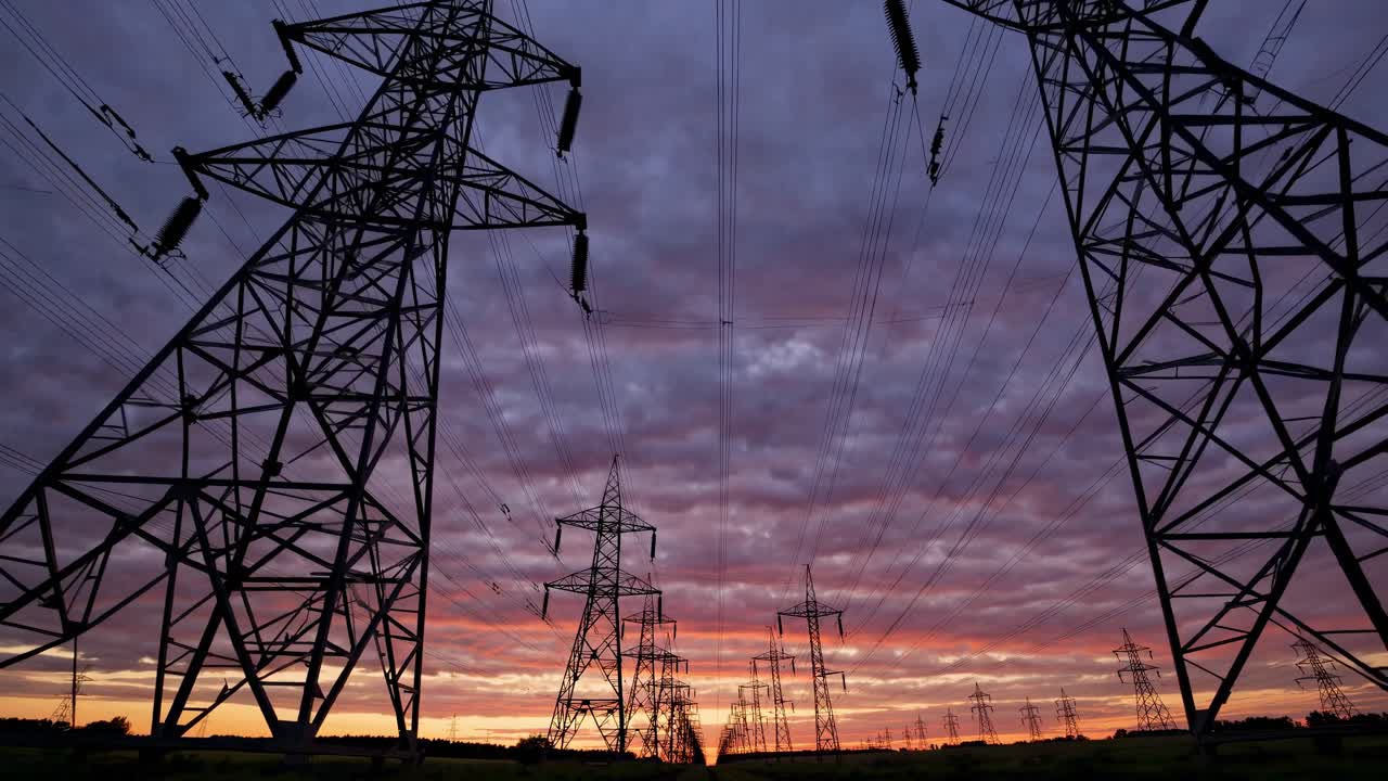 Tomada dramática em ângulo baixo de linhas de energia ao pôr do sol, capturando um céu vibrante