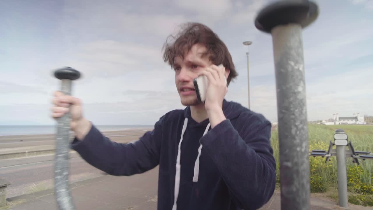 젊은이 가 드폰 을 사용 하는 동안 운동 기계 에서 운동 하고 있다