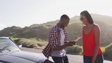 african american couple using maps for directions while standing near convertible car on road