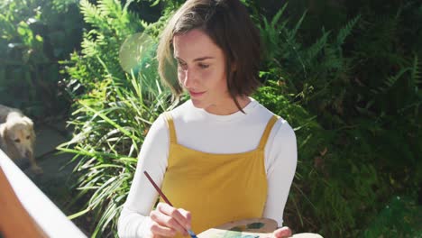 smiling caucasian woman with brown hair painting in sunny garden