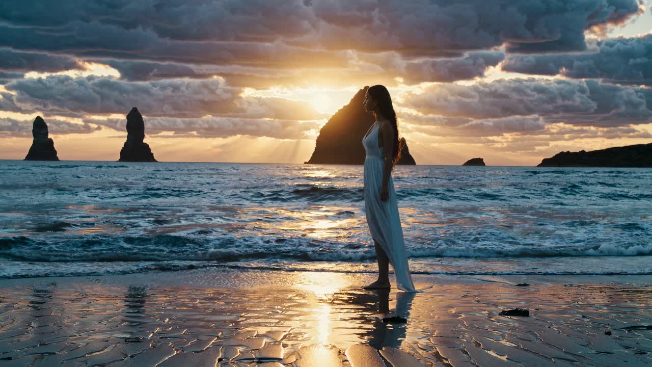 Una serena scena video di una donna in abito bianco su una spiaggia al tramonto, ripresa da un angolo basso