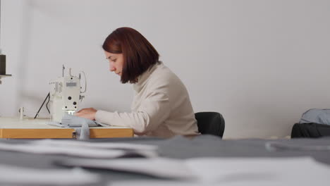 seamstress sewing fabric with industrial machine, illuminated by light for better visibility, focusing on skillful stitches, calm posture, and precise technique in bright workspace