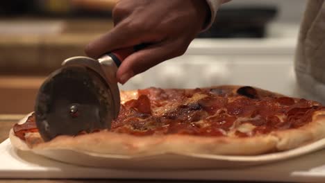 Slicing-a-freshly-baked-pepperoni-pizza-with-a-pizza-wheel-hot-out-of-the-oven---side-view