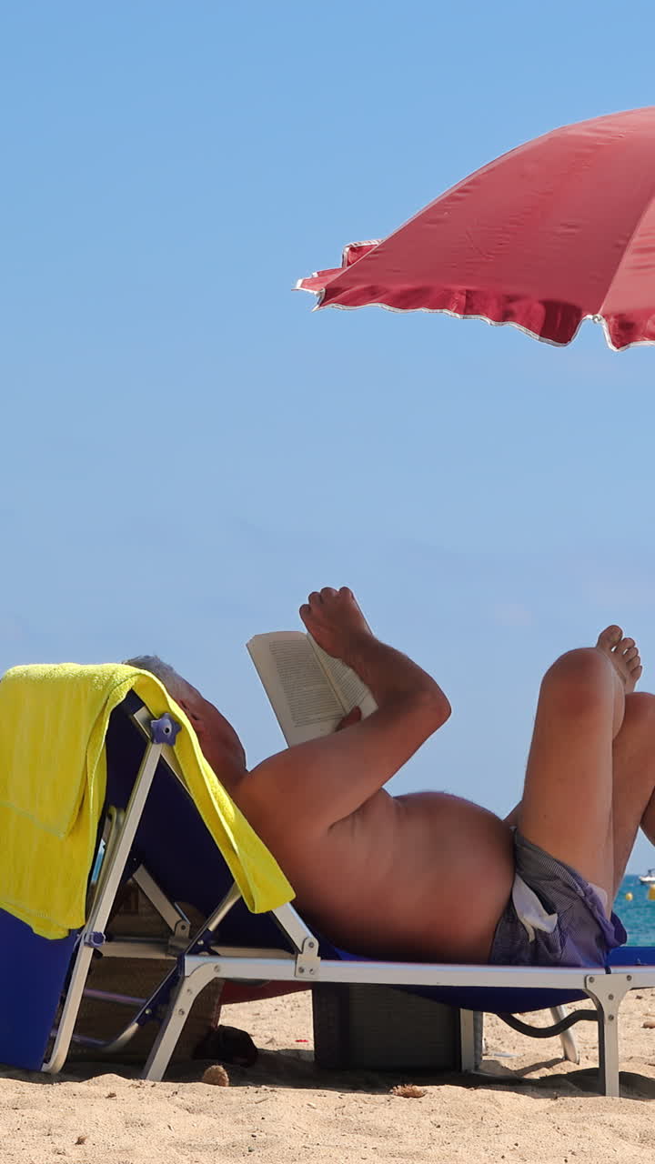 Man reading under red umbrella at the beach in Cannes, France. Vertical