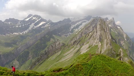 a man in a red jacket is running towards the camera on top of a mountain