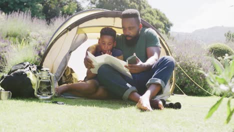 Glücklicher-Afroamerikanischer-Vater-Und-Sohn-Sitzen-Im-Zelt-Und-Lesen,-In-Zeitlupe