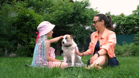 woman with daughter sitting on grass with dog