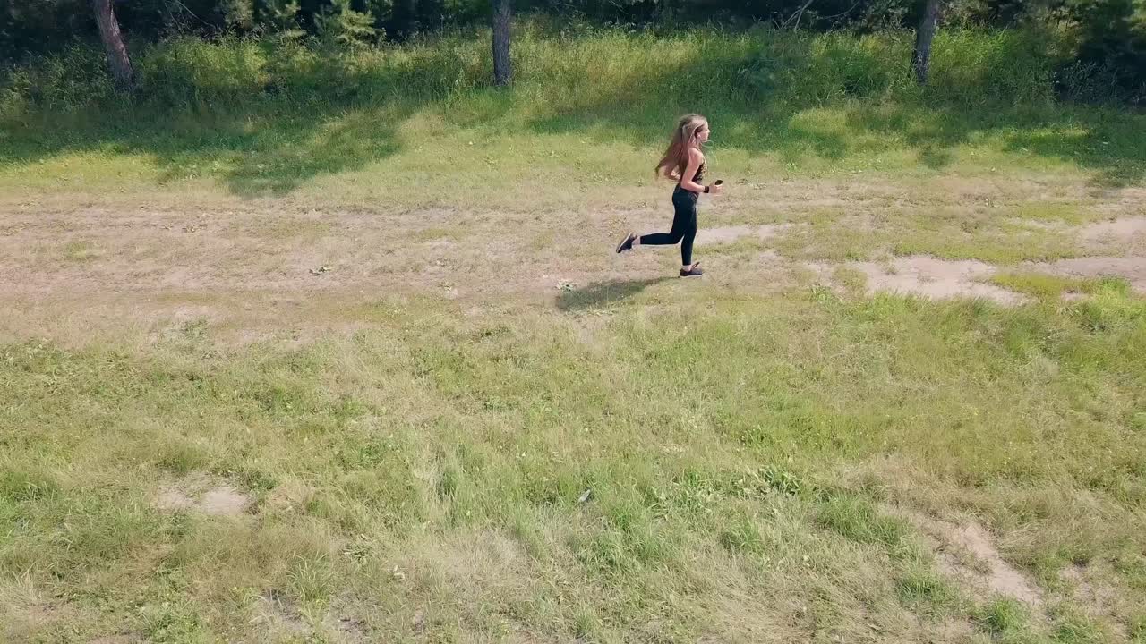 공중 촬영 추적 젊은 예쁜 소녀는 아침에 스포츠를 위해 소나무 숲과 도로를 따라 달립니다