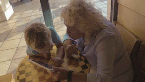 Niño-Y-Abuela-Entretenidos-Con-Panel-Táctil-En-La-Cafetería.