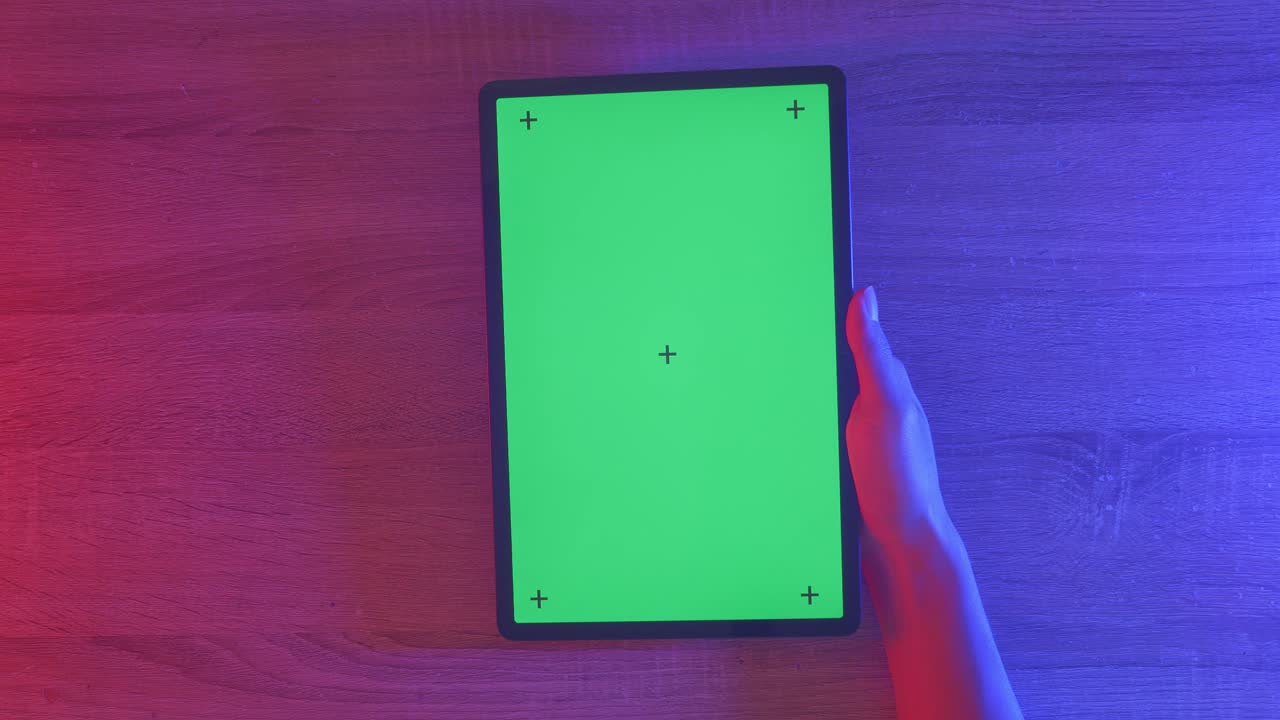 Hand met een tablet met een groen scherm op een houten tafel