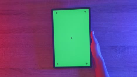 hand met een tablet met een groen scherm op een houten tafel