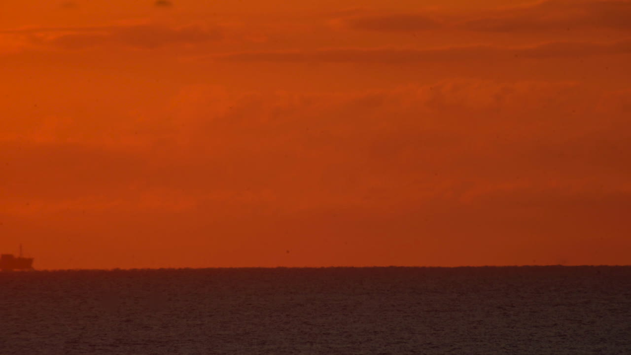 화물선이 빛나는 주황색 하늘 아래 바다 수평선을 가로질러 멀리 여행합니다.