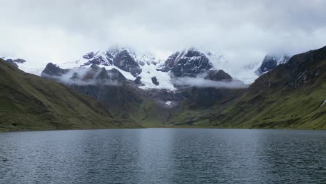 low flyover of textured laguna carhuacocha to snowy mtn peaks in peru